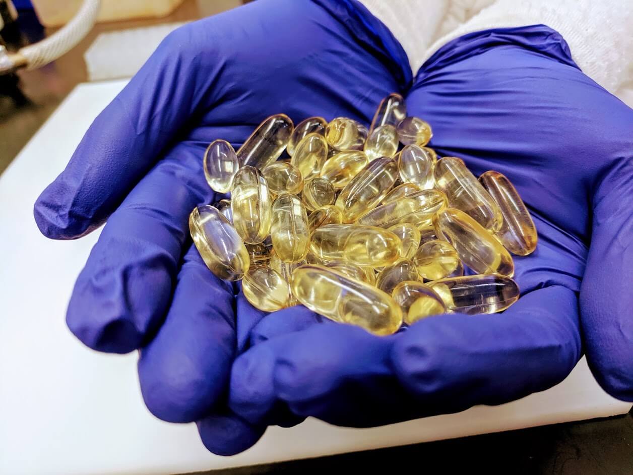 Gloved hands holding vitamin e pills in the testing laboratory